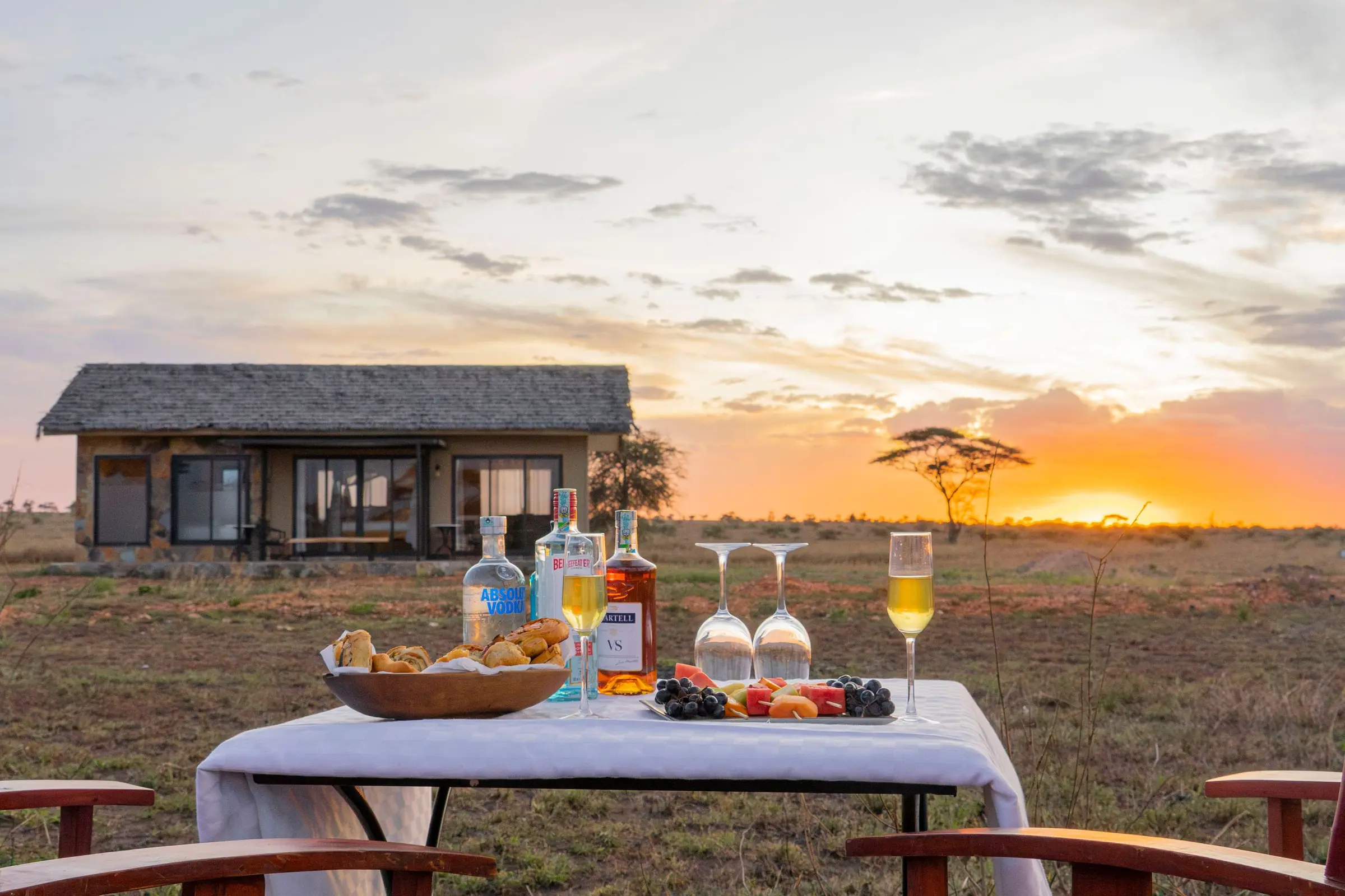 Sundowner table set on the plains, a tent and lone acacia silhouetted against a sunset sky